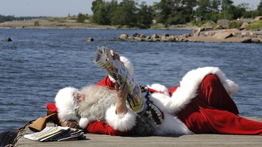 Der Weihnachtsmann ausgestreckt im Sonnenschein auf einem Bootssteg | Bild: picture-alliance/dpa