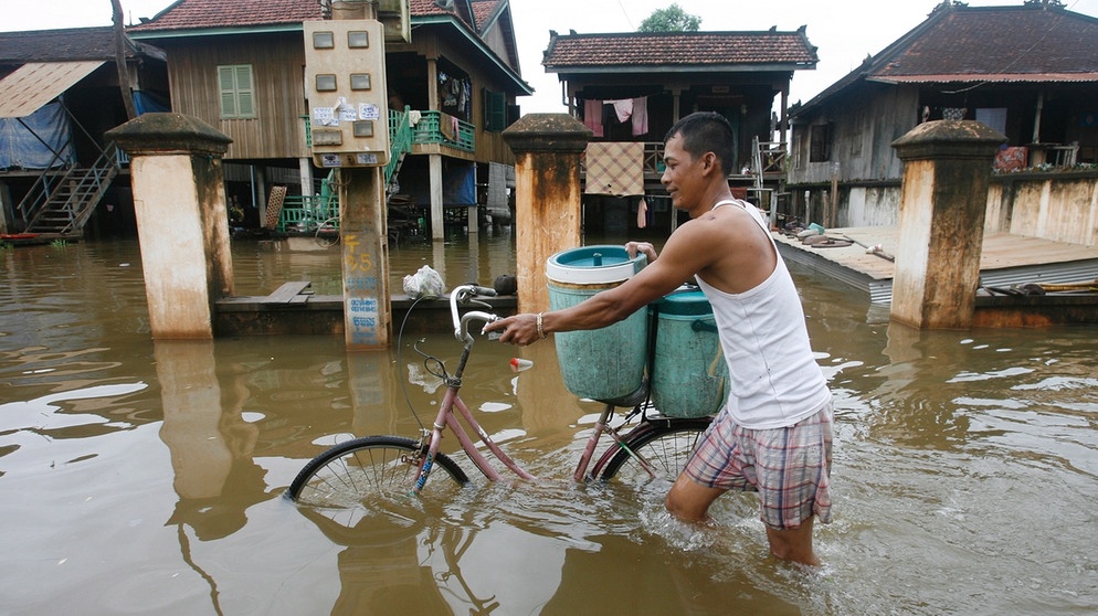 Mann schiebt Fahhrad durch überschwemmte Straße | Bild: picture-alliance/dpa