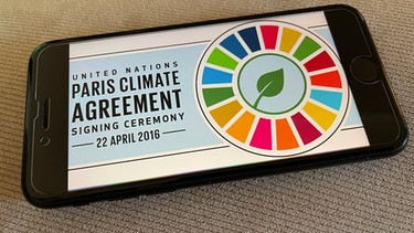 Das Logo des Klimaabkommens von Paris, abfotografiert von einem Smartphone-Bildschirm. | Bild: picture alliance / STRF/STAR MAX/IPx | STRF/STAR MAX/IPx