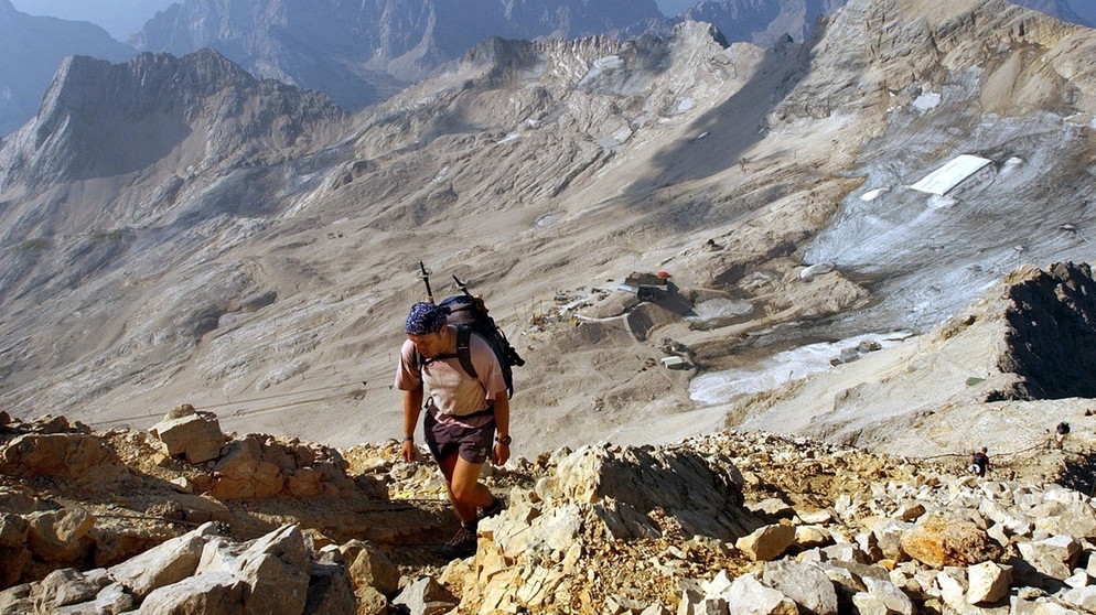 Wanderer auf der Zugspitze. Im Hintergrund ist der Rest des teilweise abgedeckten Schneeferner-Gletschers zu sehen.  | Bild: picture-alliance/dpa