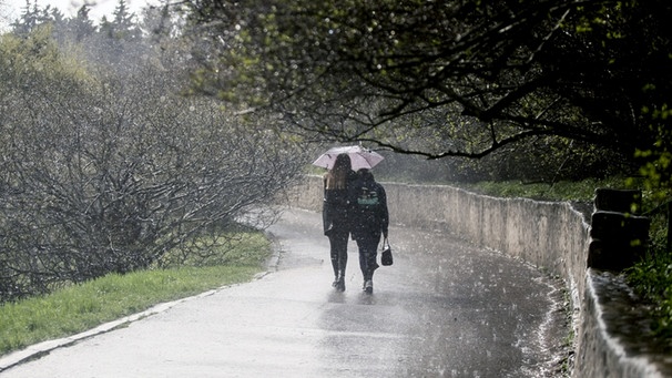 Auf diesem Bild regnet es, so viel ist klar: Die zwei Spaziergänger brauchen einen Regenschirm. Aber wie entsteht Regen eigentlich, und was ist der Unterschied zu Niederschlag, Nieselregen und Graupel? Warum klappt es mit der Wettervorhersage für Regen oft nicht gut? | Bild: picture alliance / Photoshot | -