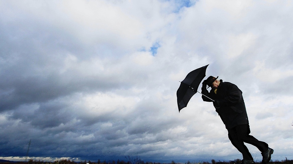 Mann kämpft mit Schirm gegen den Wind: Der Wind ist ein Wettertreiber. Der Wind beeinflusst er das Wetter, so viel ist klar. Er lässt die Sonne scheinen und treibt die Wolken an. Doch wie entstehen die Winde überhaupt? | Bild: picture-alliance/dpa