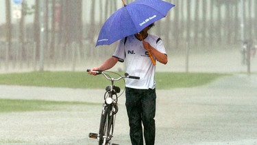 Ein Mann schiebt ein Fahrrad durch den Regen | Bild: picture-alliance/dpa