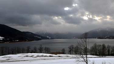 Dichte Regenwolken über dem Tegernsee, im Vordergrund: Schneereste | Bild: picture-alliance/dpa