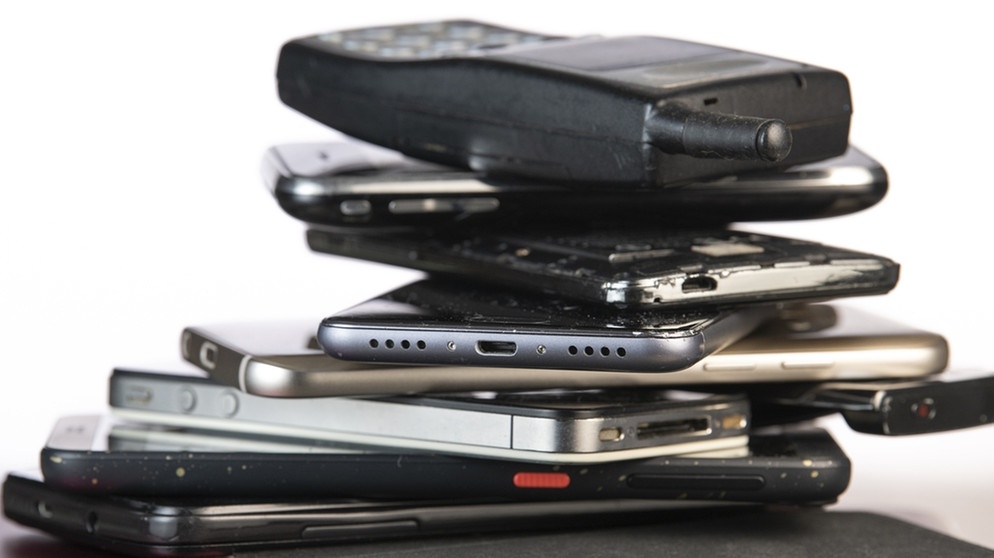 Alte Handys türmen sich auf auf einem Schreibtisch. | Bild: stock.adobe.com/FreeProd