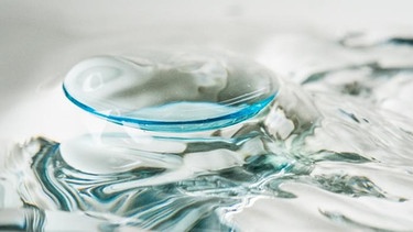 Eine Kontaktlinse schwimmt auf Flüssigkeit. Über Toilette oder Waschbecken entsorgt, landen Kontaktlinsen am Ende als Mikroplastik im Meer. | Bild: picture-alliance / dpa Themendienst