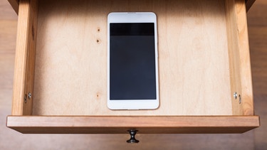 Blick von oben auf ein Smartphone, das in einer leeren Holzschublade liegt. | Bild: stock.adobe.com/vvoe