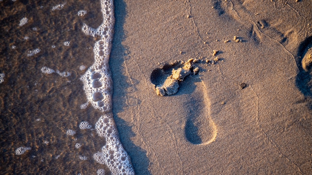 Unser Wasser-Fußabdruck ist ein Indikator, um unseren Wasserverbrauch auch bei Konsumgütern in den Blick zu bekommen; Fußabdruck im nassen Sand. | Bild: picture alliance/dpa/dpa-Zentralbild | Stefan Sauer