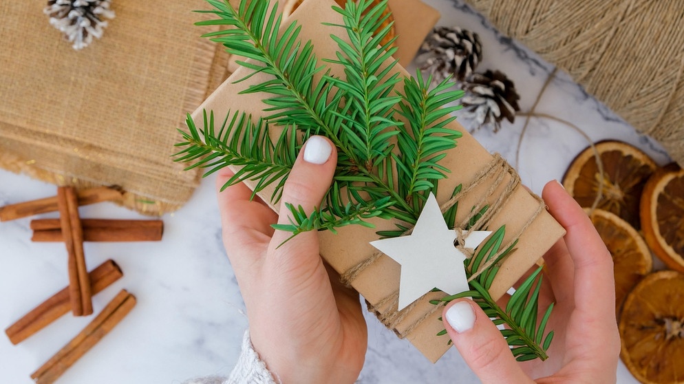 Ein Geschenk ist in Papier eingewickelt. Dafür eignen sich beispielsweise Papiertüten aus dem Supermarkt. Das Geschenk könnt ihr auch mit Zweigen, Beeren oder wiederverwehrteten Holzschmuck schmücken. Geschenkpapier ist oft schädlich für Klima und Umwelt. Wir verraten euch Tipps, wie ihr Geschenke an Weihnachten nachhaltig und umweltfreundlich verpackt.  | Bild: picture-alliance/dpa