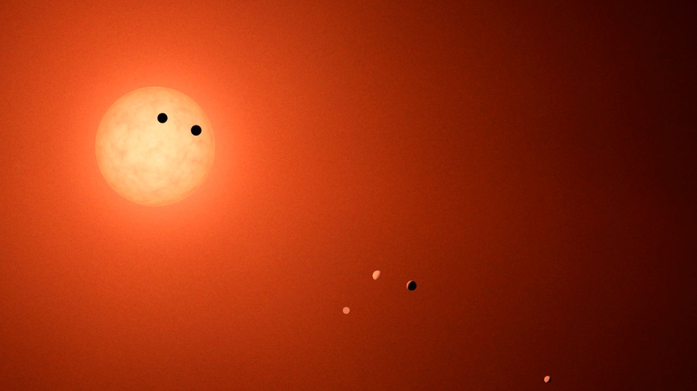 Trappist 1 ist ein Sternsystem, von dem Astronomen wissen, dass mehrere Exoplaneten den Zentralstern umrunden. In einigen tausend Jahren könnte die Erde von dort aus sichtbar sein, wenn sie - von dem Sternsystem Trappist 1 aus gesehen - an der Sonne vorüberzieht. Dann sind die geometrischen Bedingungen im Weltraum günstig.  | Bild: NASA/JPL-Caltech/R. Hurt (IPAC)