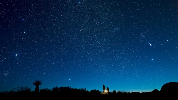 Zwei Menschen betrachten den Sternenhimmel. Am Himmel ist die Konstellation von Orion zu erkennen. Orion ist eine offiziell anerkannte Konstellation der Internationalen Astronomischen Union (IAU).  | Bild: picture alliance / All Canada Photos | David Nunuk