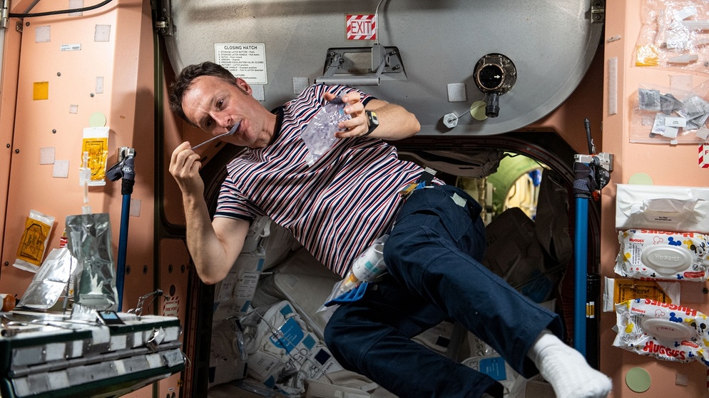 Astronaut Matthias Maurer in Ringelshirt beim Frühstücken auf der ISS, er hängt schräg im Foto, mit einem Löffel im Mund.  | Bild: ESA