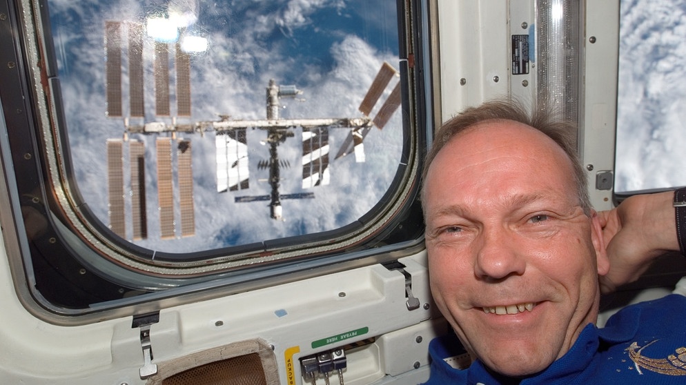 Der Astronaut Hans Schlegel 2008 vor dem Fenster des Space Shuttles Atlantis, im Hintergrund ist die ISS  zu sehen. Er war einer der deutschen Astronauten, die schon vor Alexander Gerst ins Weltall geflogen sind. | Bild: NASA