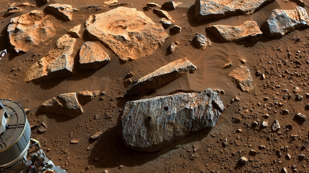 Ein Stück Marsgestein, zwei Löcher: Im September 2021 hat der Mars Rover Perseverance erstmals erfolgreich Gesteinsproben auf dem roten Planeten eingesammelt. In einen Stein bohrte der Rover zwei Löcher und füllte zwei Probenröhrchen mit dem Material. Zu einem späteren Zeitpunkt könnte dies im Rahmen einer Mars Sample Return Mission abgeholt werden.  | Bild: NASA/JPL-Caltech