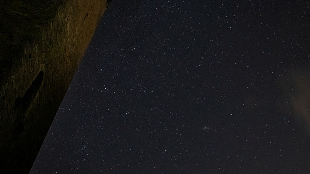 Das markante W des Sternbilds Kassiopeia ist hier dicht neben dem Würzburger Schenkenturm zu sehen. Der schimmernde Fleck rechts darunter ist der Andromedanebel M31 (Andromedagalaxie) im Sternbild Andromeda. Aufgenommen im August 2019 von Michael Deisinger  | Bild: Michael Deisinger