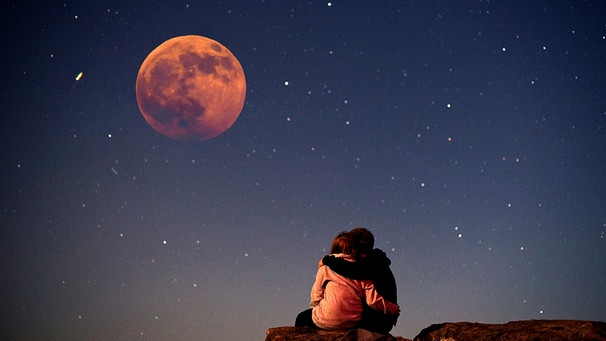 Sterngucker beobachten eine totale Mondfinsternis: Ein Pärchen betrachtet eng umschlungen den abendlichen Sternenhimmel voller Sterne und dem Blutmond bei einer MoFi (Collage) | Bild: pa/dpa; Montage: BR