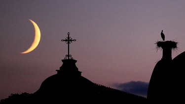 Die schmale, zunehmende Mondsichel mit Storchennest auf dem Kloster Benediktbeuern. Aufnahme vom 22.07.2012 um 21.37 Uhr. | Bild: Walter Seibold