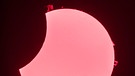 Foto der partiellen Sonnenfinsternis, die am 25. Oktober 2022 zu sehen war, fotografiert mit einem H-alpha Sonnenteleskop von Marco Sproviero in München. So ein Teleskop lässt nur den Teil sichtbaren Lichts durch, der der Wellenlänge des ionisierten Wasserstoffs entspricht: 656,28 Nanometer. So werden Protuberanzen und die Oberflächenkonturen der Sonne sichtbar. | Bild: Marco Sproviero