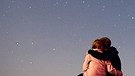 Sterngucker: Ein Pärchen betrachtet eng umschlungen den abendlichen Sternenhimmel voller Sterne | Bild: picture-alliance/dpa