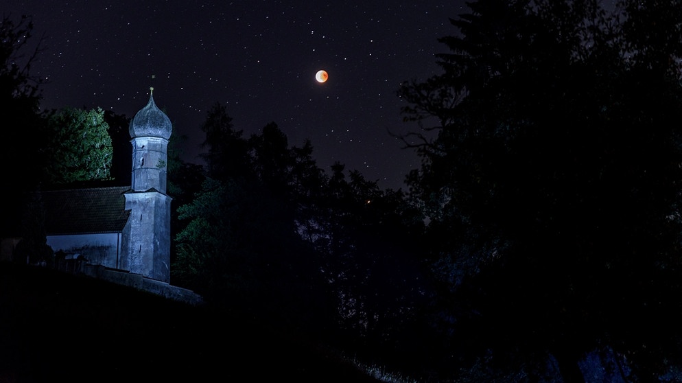 Die totale Mondfinsternis am 27.07.2018 am Egglburger See, der Mars ist durch die Bäume auch zu sehen. Im Vordergrund eine Kirche. | Bild: Ernst Schindler